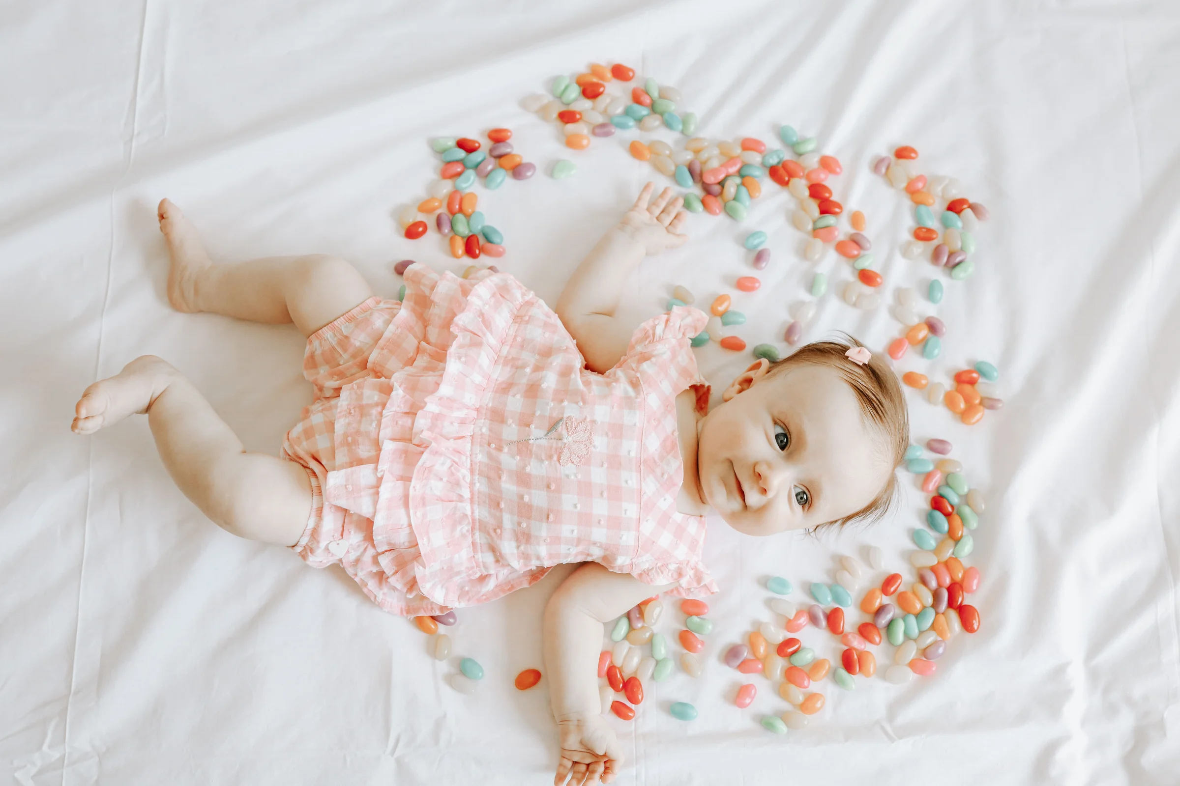 Baby lying on a white sheet surrounded by colorful jellybeans, playful portrait
