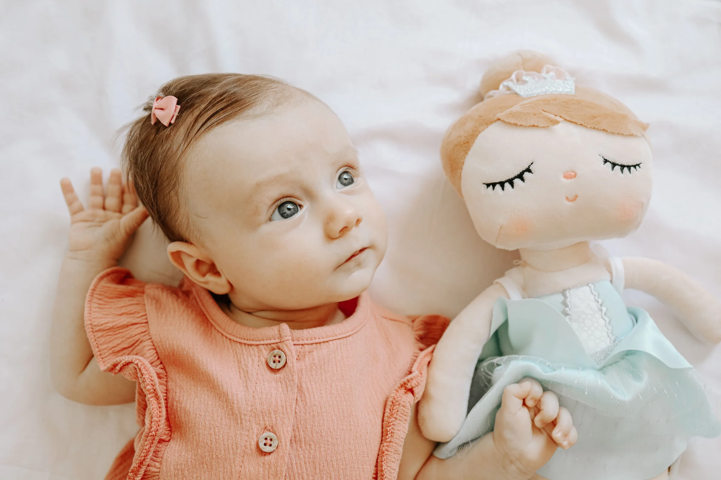 Close up portrait of a baby lying next to a soft toy doll