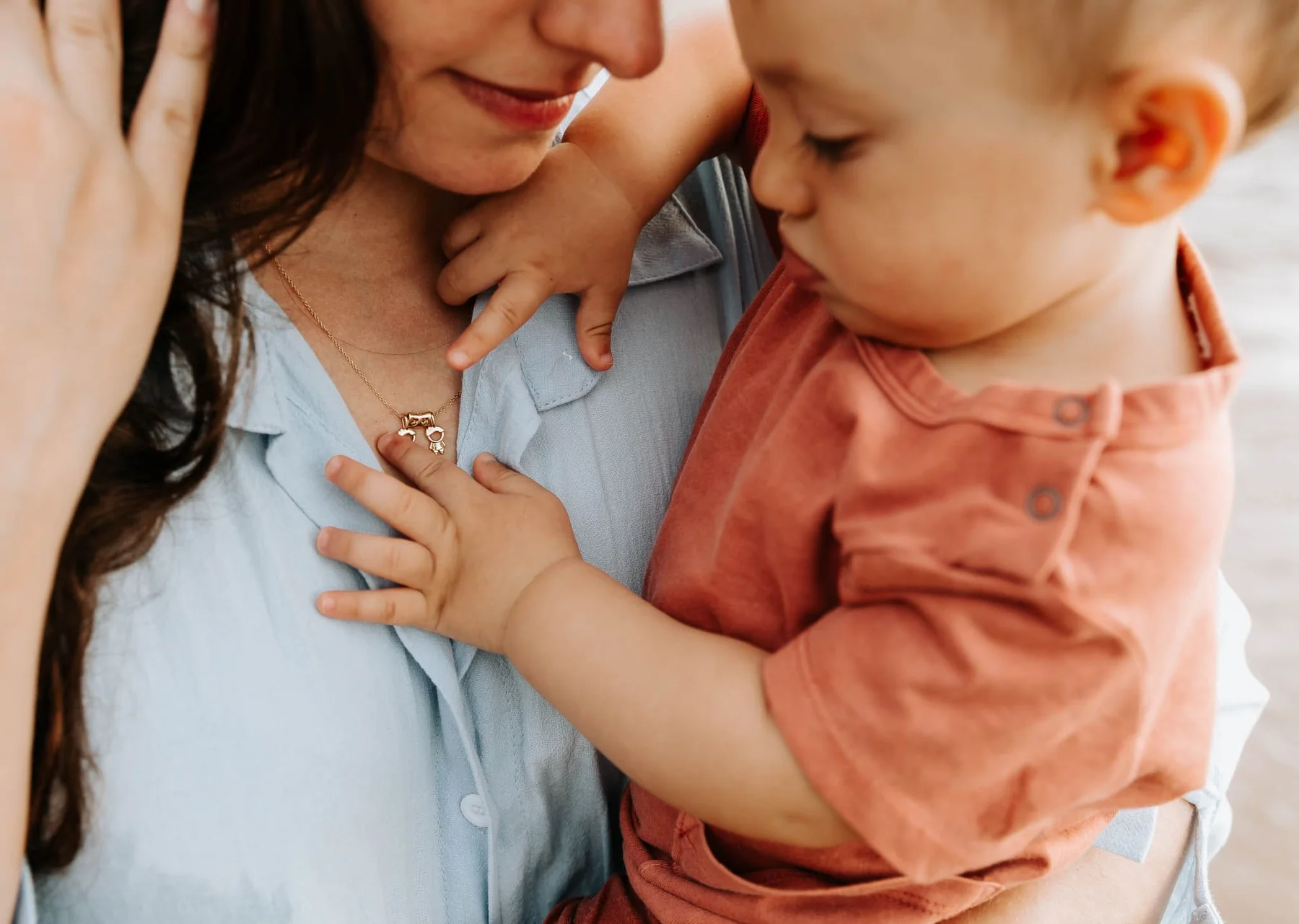 Close up of a toddler reaching for mom's necklace, lifestyle family portrait