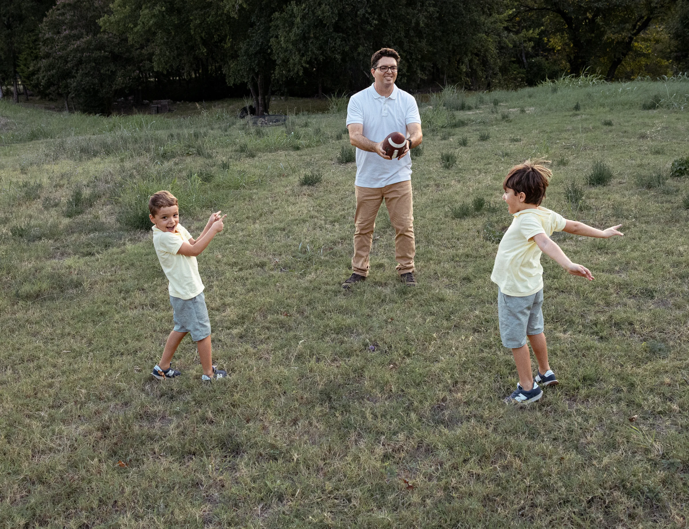 Father holding a football with two boys in yellow shirts playing in a grassy field, outdoor family session