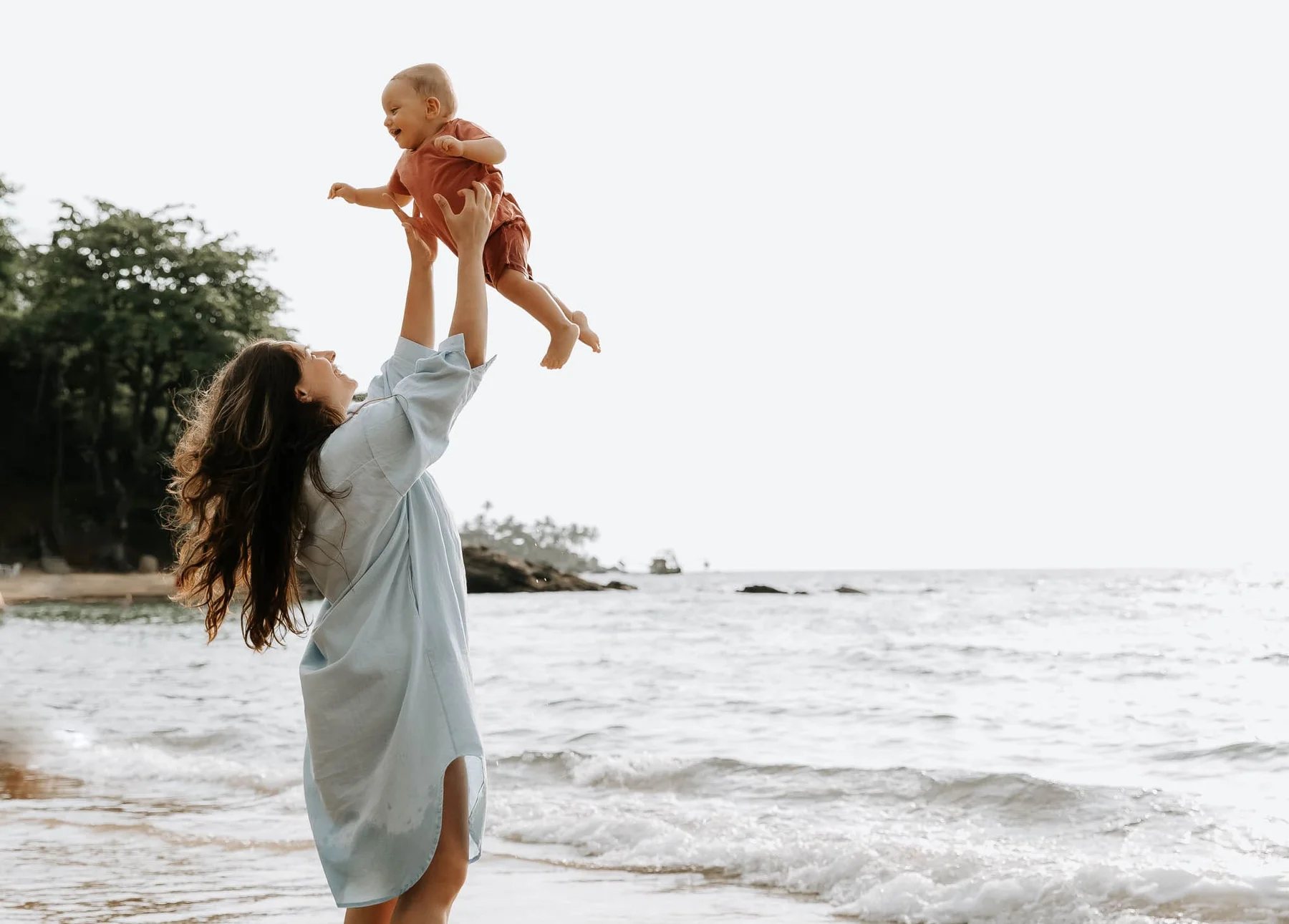 Mother lifting her laughing baby up in the air at the beach