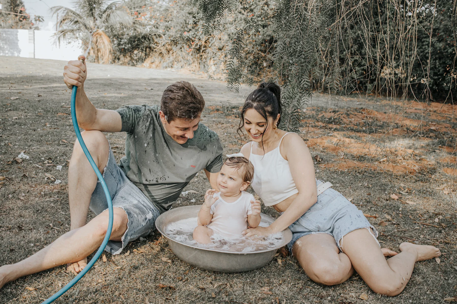 Parents giving their toddler a playful outdoor bath at home