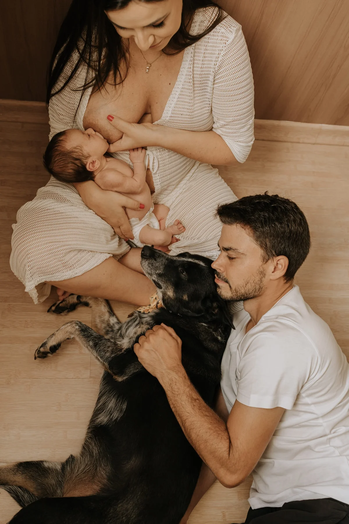 Mother nursing her newborn on the floor at home while the family dog looks on