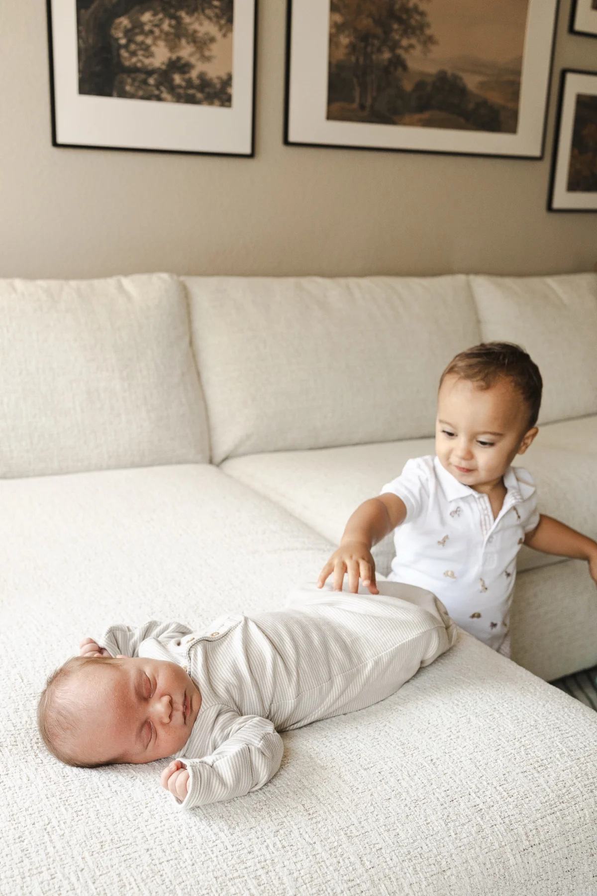 Newborn asleep on the sofa while the toddler sibling reaches over, in home newborn session